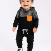 Smiling toddler in a black baby hoodie and jogger set with white stripes and a mustard pocket.